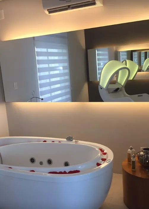 Banheira de hidromassagem com pétalas de rosa vermelhas e lavatório iluminado ao fundo