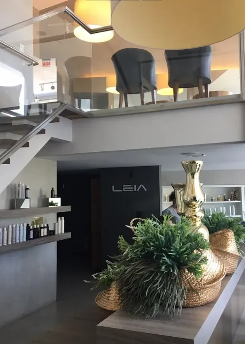 Casa de Florianópolis: pé-direito duplo com mezanino de vidro, poltronas, logo Leia na parede escura e vaso dourado